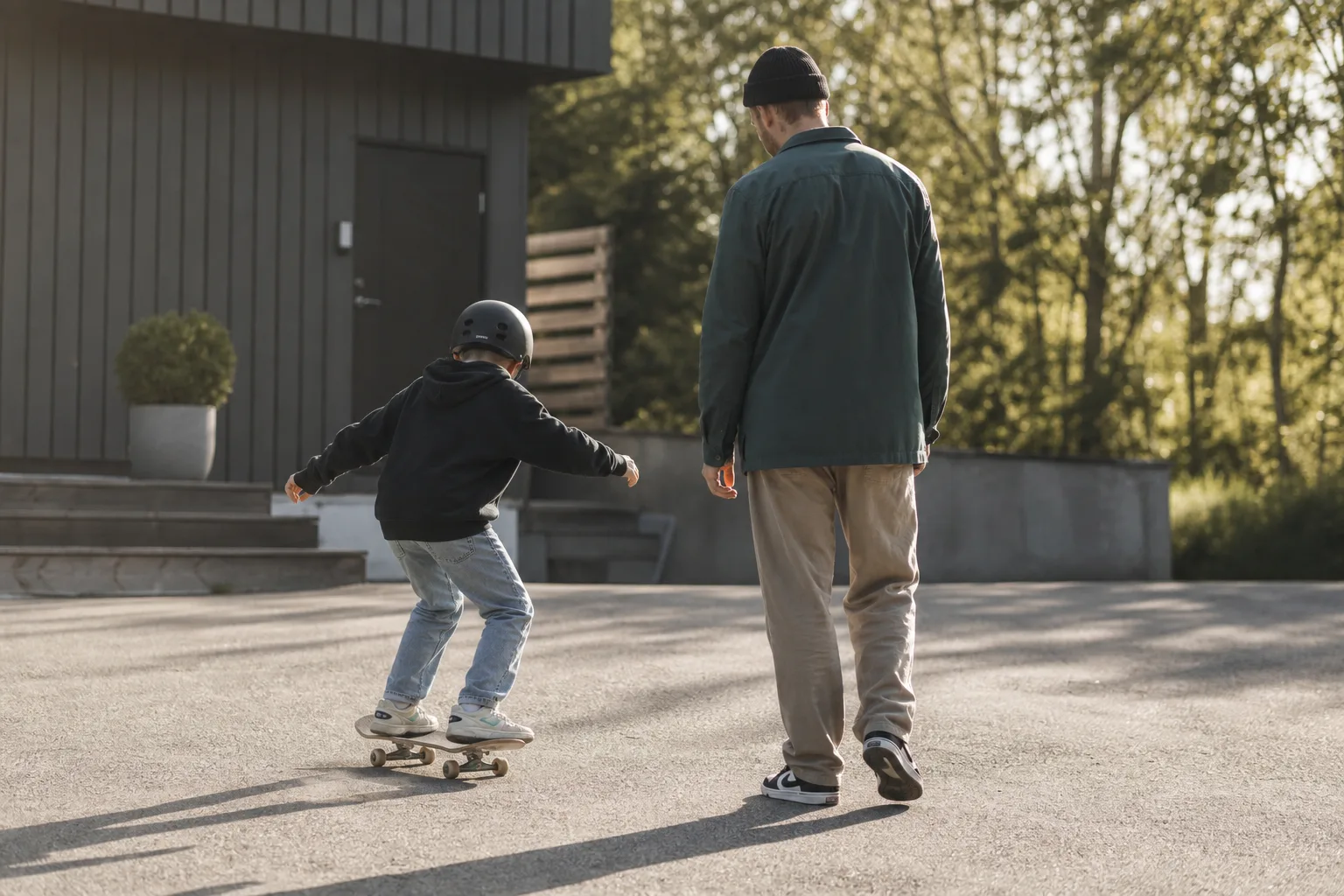 Ett barn övar balans på en skateboard med en vuxen bredvid på en gårdsplan