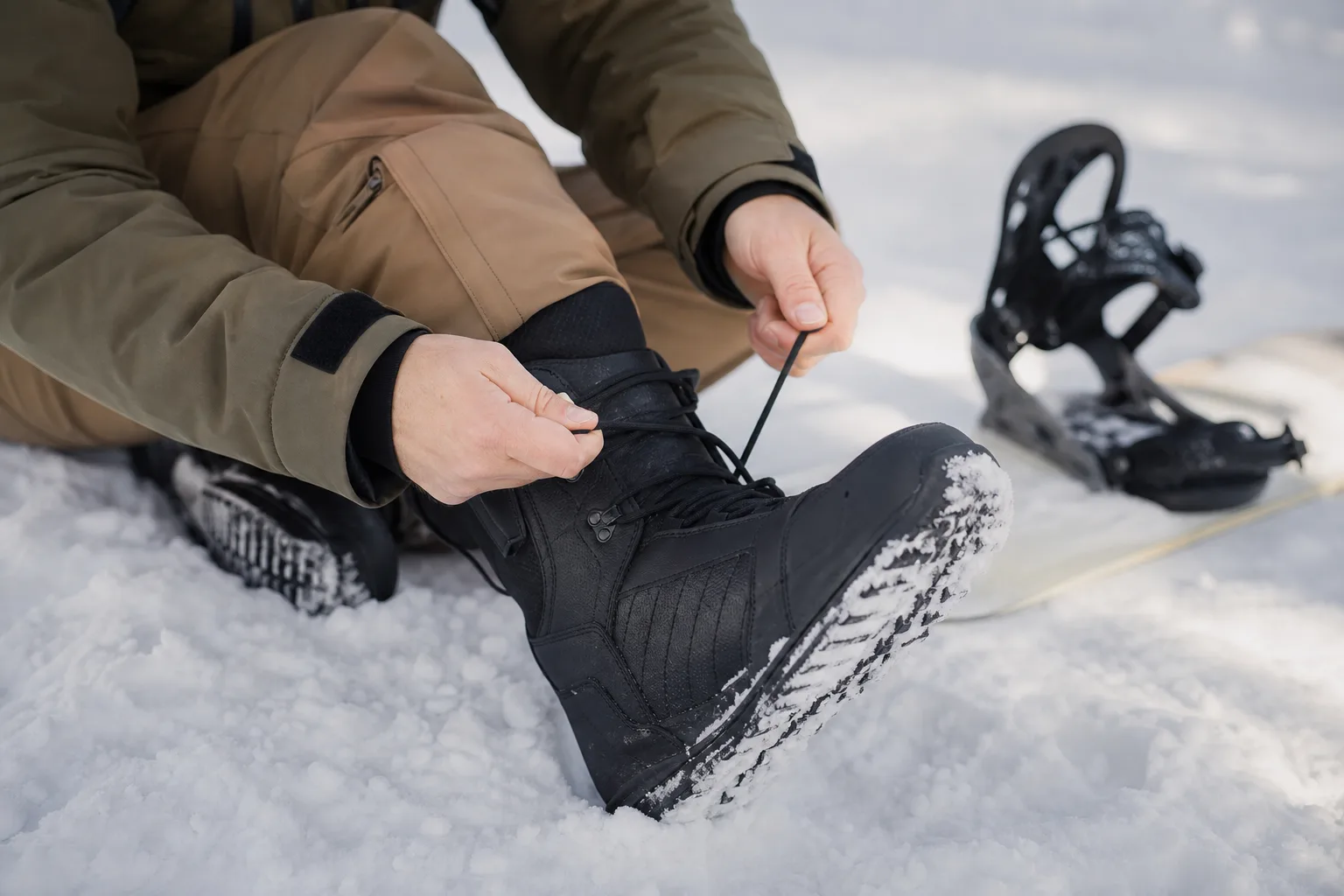 Person som snör en snowboardboot i snön