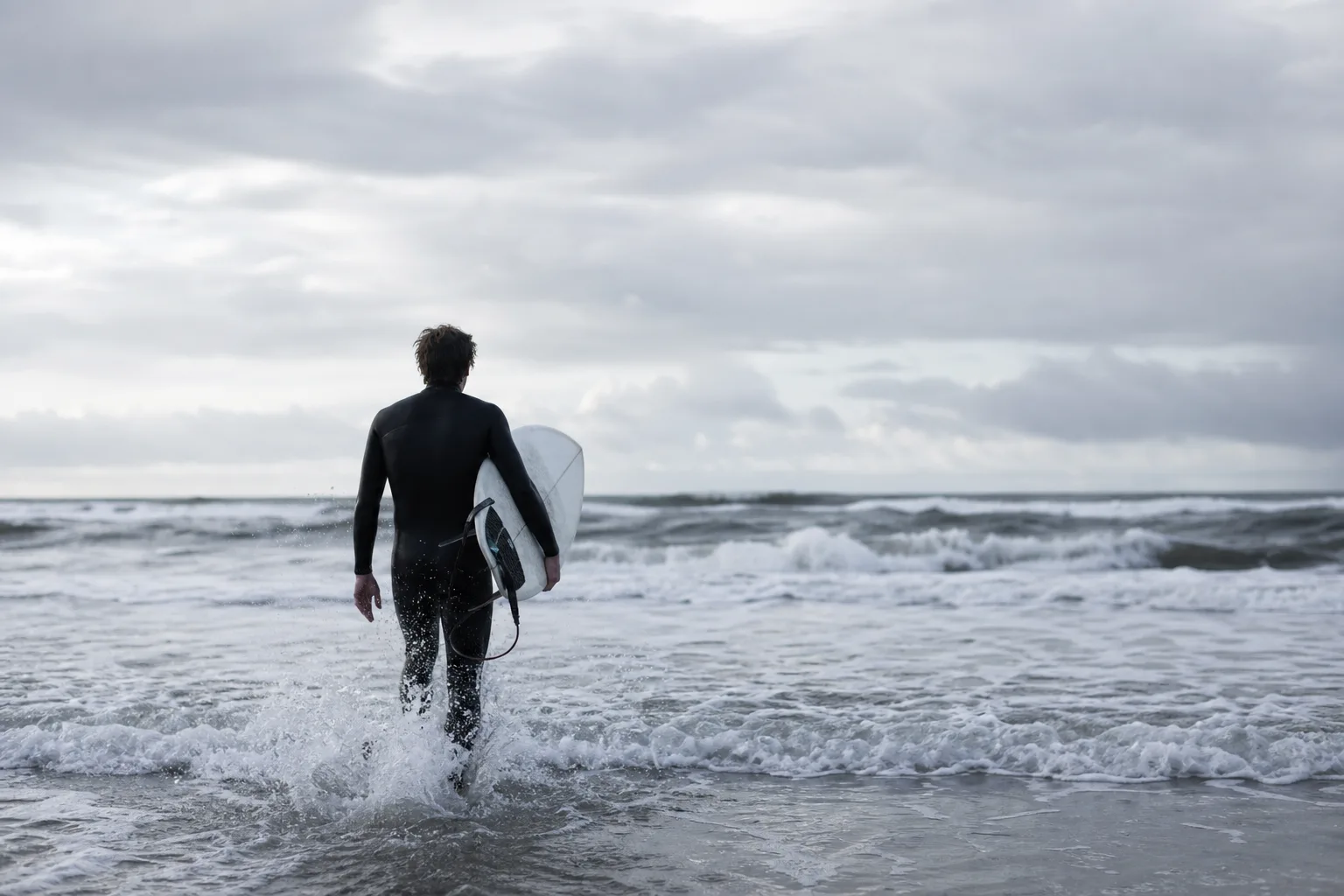 Person i våtdräkt som vadar ut i vitvatten med surfbräda under armen