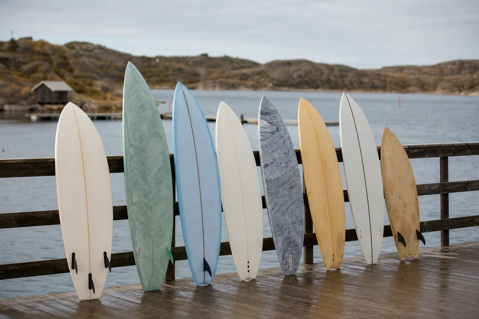 Flera olika surfbrädor lutade mot ett träräcke vid en hamn