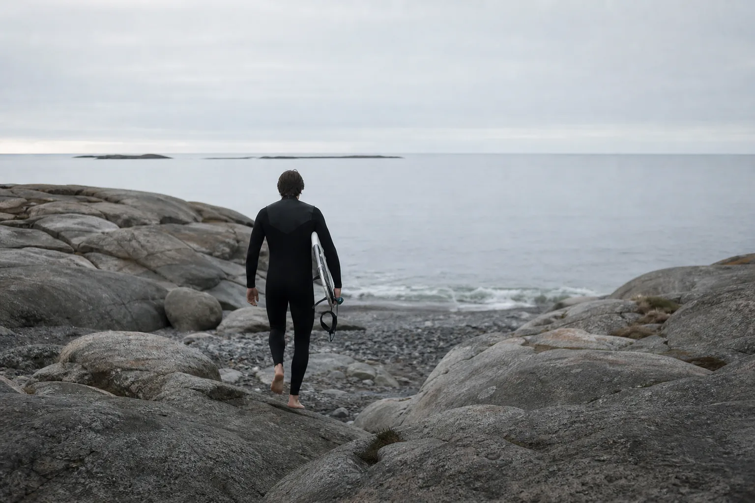 Person i våtdräkt sedd bakifrån på väg ner mot en stenstrand